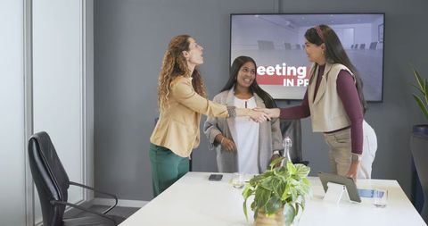 Three Women Shaking Hands in Modern Boardroom During Professional Meeting