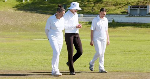 Female Cricket Umpire and Players Inspecting Ball on Pitch