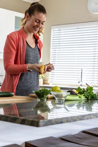 Smiling woman peeling banana while meal prepping on modern minimalist clean kitchen island