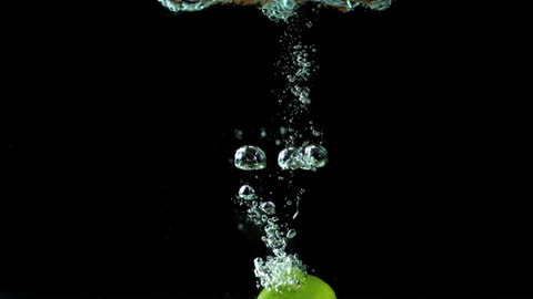 Green Lime Falling into Water with Bubbles against Black
