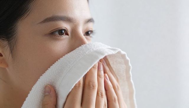 Closeup asian woman pressing white towel to lower face during skincare routine