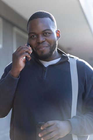 African american commuter talking on phone holding coffee wearing shoulder strap bag