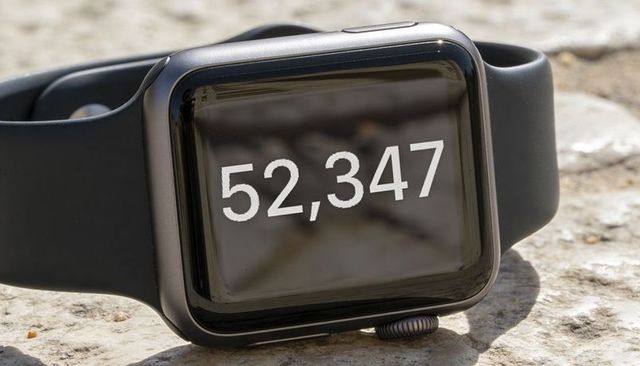Square smartwatch displaying step count 52,347 on glossy screen, closeup outdoor detail