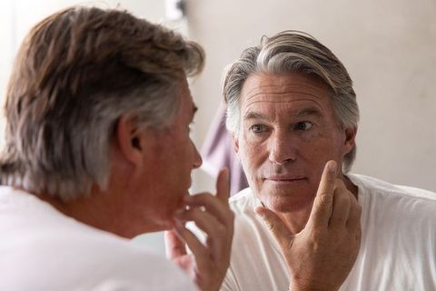 Mature man examining face in mirror morning skincare grooming routine closeup