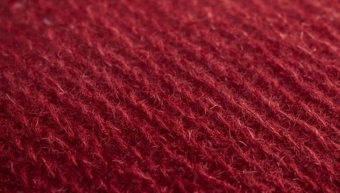 Macro red knit texture showing diagonal stitches, fuzzy fibers and pile detail