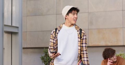 Diverse male students checking phones on urban campus with backpacks and notebooks