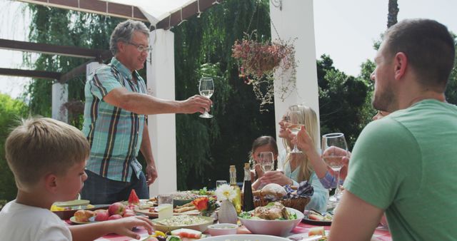 Happy caucasian family sitting at table in garden, eating dinner and making a toast. Lifestyle, domestic life, family, and togetherness.