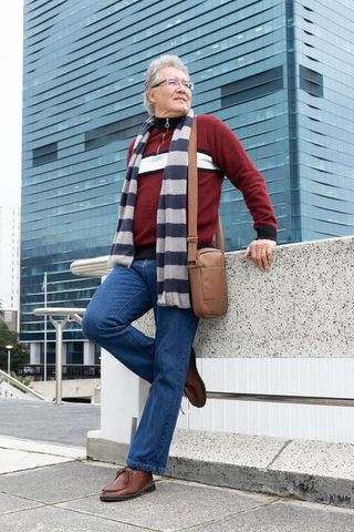 Senior asian man standing in city plaza wearing striped scarf and leather crossbody bag