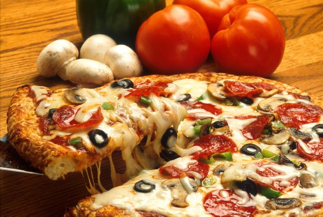 Freshly baked veggie and pepperoni pizza with a delicious cheese pull. Ingredients like mushrooms, bell peppers, and tomatoes are in background. Perfect for use in advertisements for pizza restaurants, food blogs, menus, or culinary magazines.