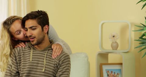 Woman whispering secret to boyfriend sitting on couch