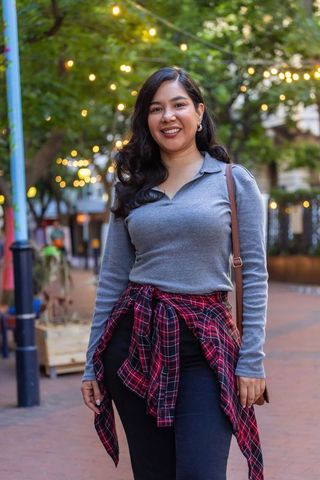 Smiling woman standing on urban brick street with warm bokeh string lights at dusk