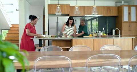 Multigenerational women cooking together in modern sunlit kitchen preparing family meal