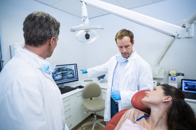 Dentists explaining dental x-ray results to a female patient in a modern dental clinic. The image can be used for healthcare websites, dental care promotions, patient education materials, and medical consultation services.