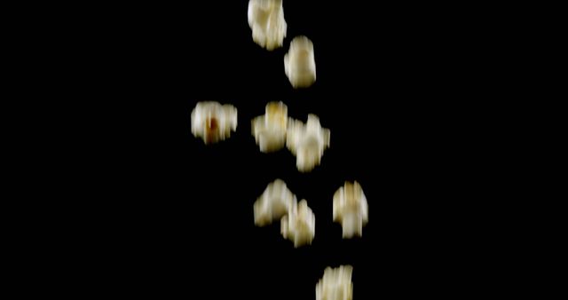 Popcorn kernels falling in mid-air against a black background, showcasing the action and simplicity of this popular snack. Useful for promoting cinema experiences, food blogs, snack-related products, or any concept related to entertainment and casual eating.