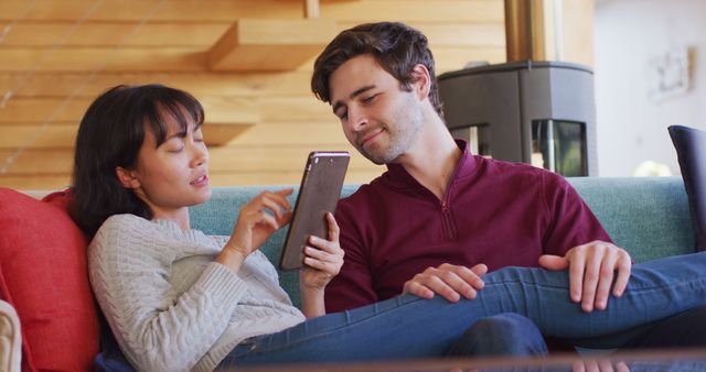 Image of back view of happy diverse couple sitting on sofa with smartphone. Love, relationship and spending quality time together concept.