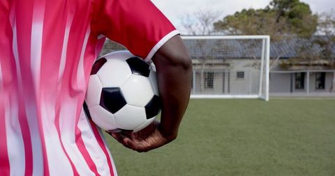 Person Holding Soccer Ball on Green Field Near Goal