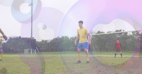Holding position youth player standing on muddy soccer pitch with goalkeeper in background