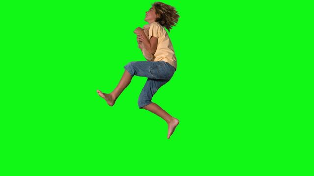 A young boy captured mid-jump, enthusiastically reaching out to catch a plush teddy bear against a green screen background. This dynamic and lively composition can be used for playful children's content, advertisements reflecting youthful energy, or as a creative element needing a chroma key setting for diverse visual effects.