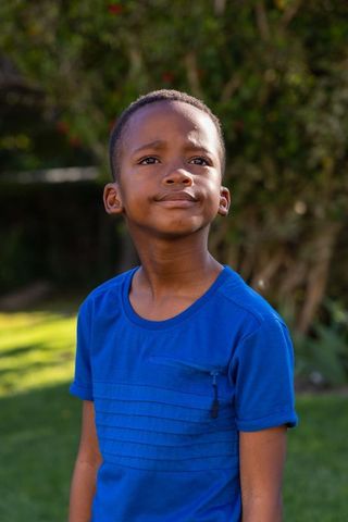 African american boy standing in sunlit garden gazing upward with thoughtful expression