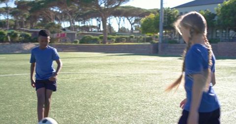 Youth players dribbling soccer ball on sunlit turf field showing teamwork and training