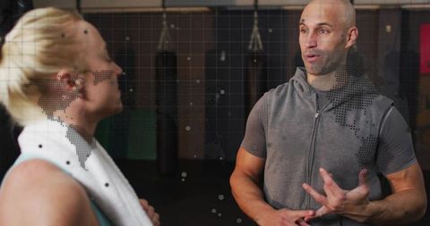 Fitness coach coaching female client in gym, gesturing technique with punching bags
