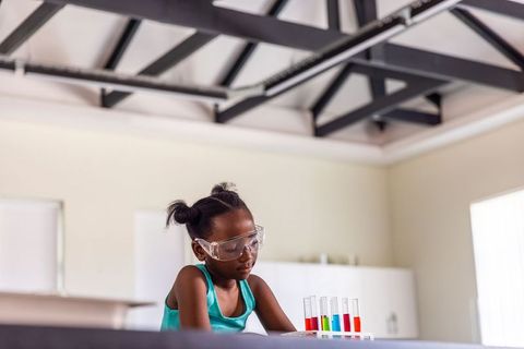 African american girl conducting colorful chemistry experiment wearing safety goggles in lab