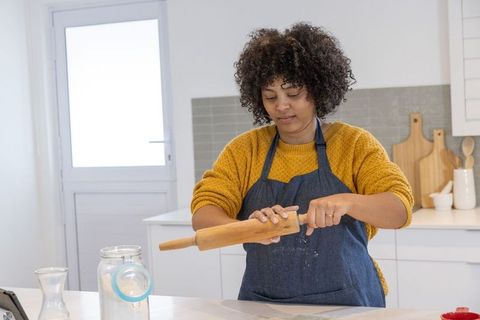 African american woman rolling dough with rolling pin in bright home kitchen for baking