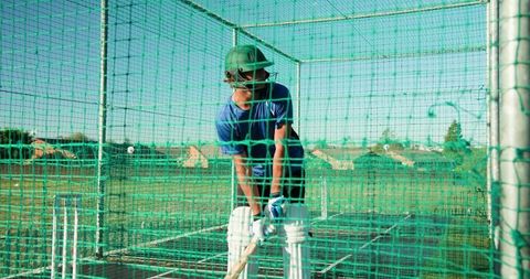 Cricket batsman practicing in green net wearing helmet and pads during outdoor training