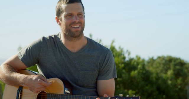 Smiling caucasian man sitting outside in sun playing acoustic guitar, copy space - Download Free Stock Photos Pikwizard.com