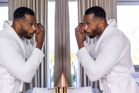 African american man grooming at bathroom mirror in white bathrobe during morning routine