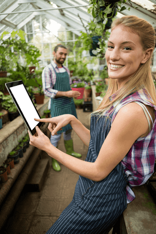 Smiling Gardener Demonstrating Tablet in Transparent Greenhouse