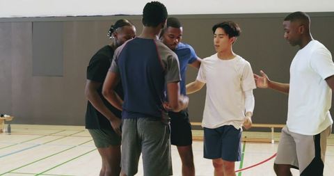 Multiracial male teammates bumping fists and huddling on indoor basketball court