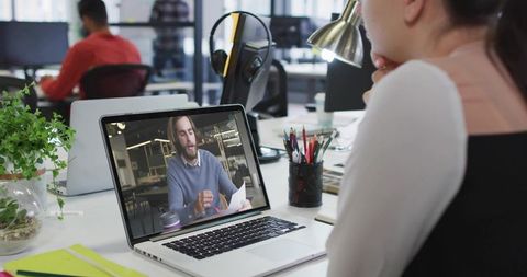 Woman watching video call with bearded coworker on laptop in open office workspace