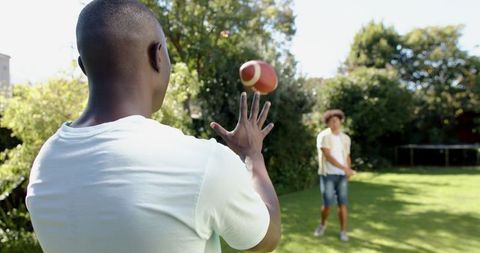 Friends Enjoying Catch with American Football in Sunny Backyard