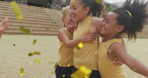 Joyful Schoolgirls Celebrating Victory with Gold Confetti Outdoors