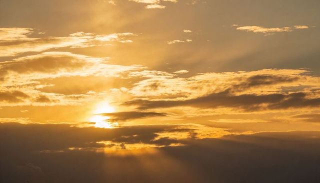 Golden dawn sun peeking through layered clouds casting crepuscular rays over horizon