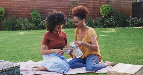 African American women sitting on pink blanket in backyard pouring water from pitcher