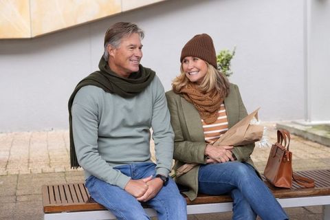 Mature couple enjoying autumn outing on bench holding bouquet and smiling