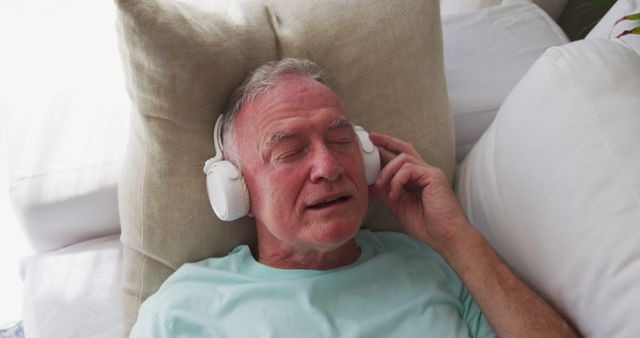Caucasian senior man wearing headphones singing while lying on the couch at home. staying at home in self isolation in quarantine lockdown