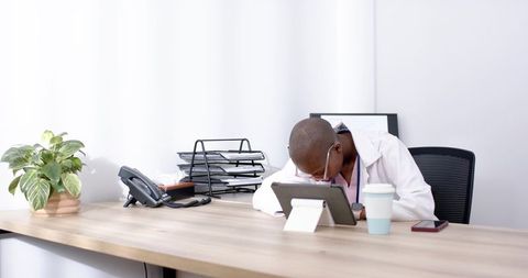 Tired medical professional resting head on desk using tablet reviewing patient records