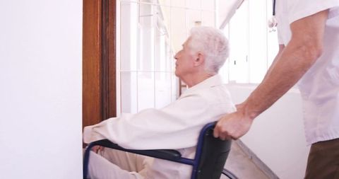 Nurse pushing elderly man in wheelchair down bright corridor, providing compassionate care