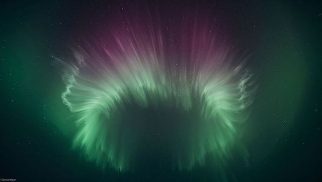 Glowing auroral corona streaming through starry sky with green curtains and magenta halo