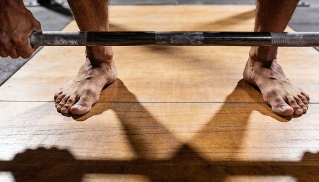 Barefoot weightlifter gripping barbell on wooden platform showing strength and focus