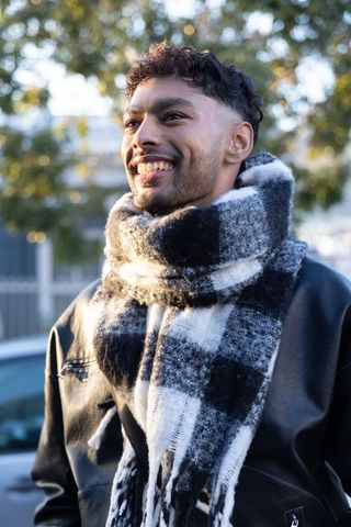 Smiling man wearing checkered scarf and leather jacket looking upward on urban street