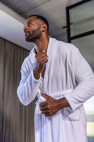 Mature african american man applying deodorant in white robe for luxury morning grooming