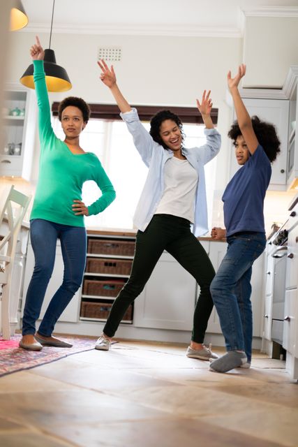 Biracial lesbian couple and daughter having fun dancing in kitchen. enjoying time together at home in self isolation during coronavirus covid 19 pandemic.