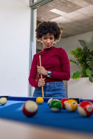 African american woman playing pool at blue felt table holding cue stick watching shot