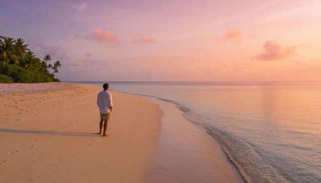 Man walking along tropical beach at sunset leaving footprints on smooth sand