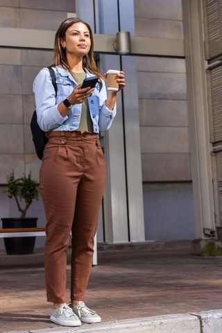 African american woman standing with smartphone and takeaway coffee outside office