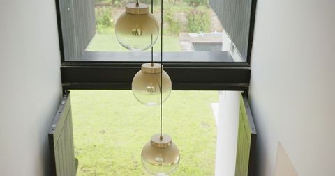 Minimalist glass pendant lamps before large window with garden view